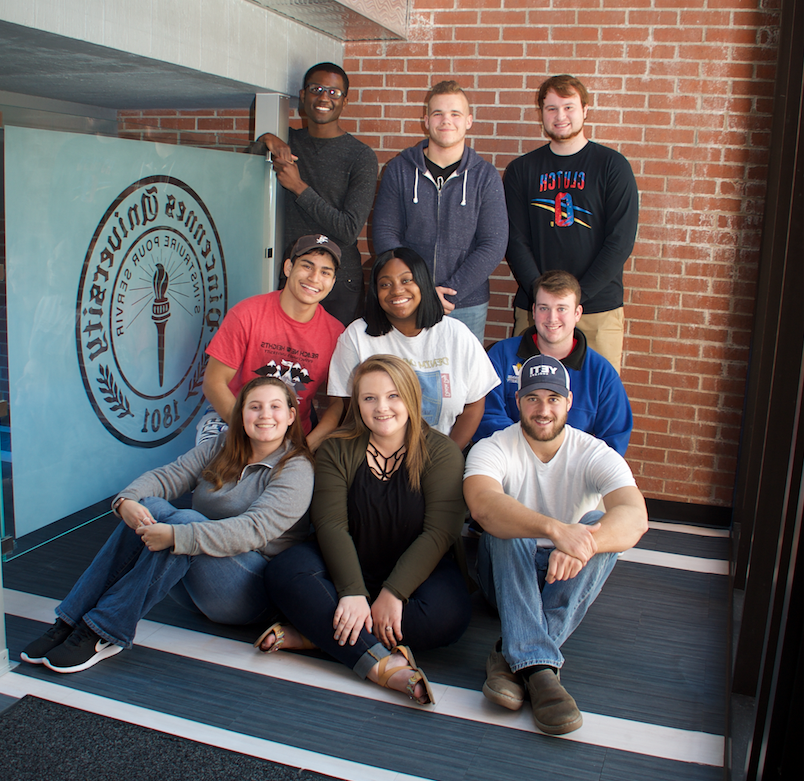 A group of students sitting in front of a brick wall